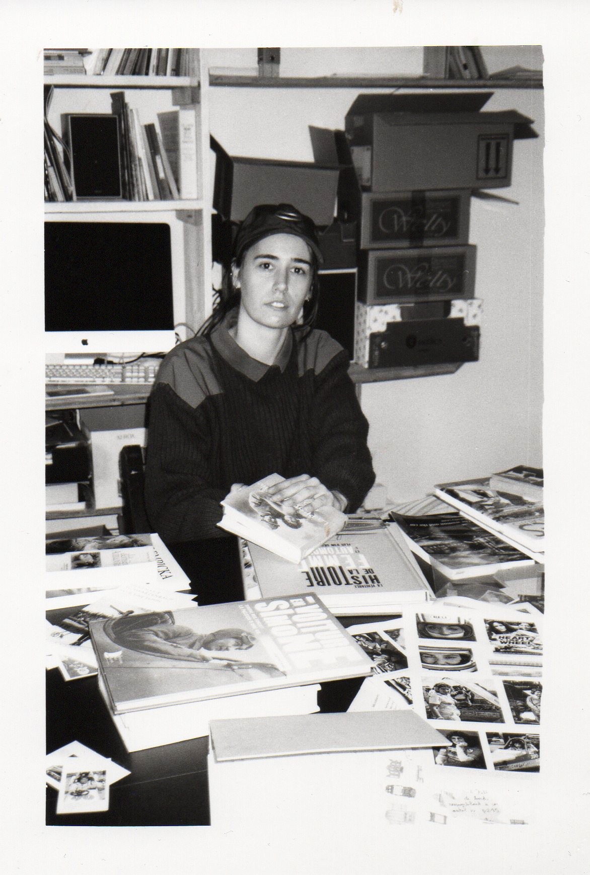 Portrait en noir et blanc de Justine Siret dans son atelier, entourée de livres, de photographies et de documents.